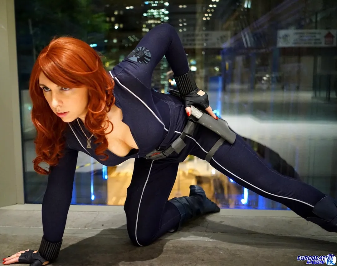 Jerikandra as Black Widow from Iron Man 2 in a navy catsuit with holster, crouched low in a city setting at dusk.
