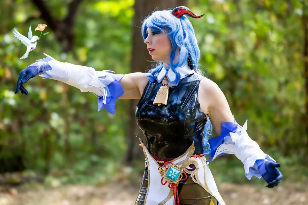 Jerikandra as Ganyu from Genshin Impact with blue hair and horns, in a black and white outfit, arms outstretched in a forest.