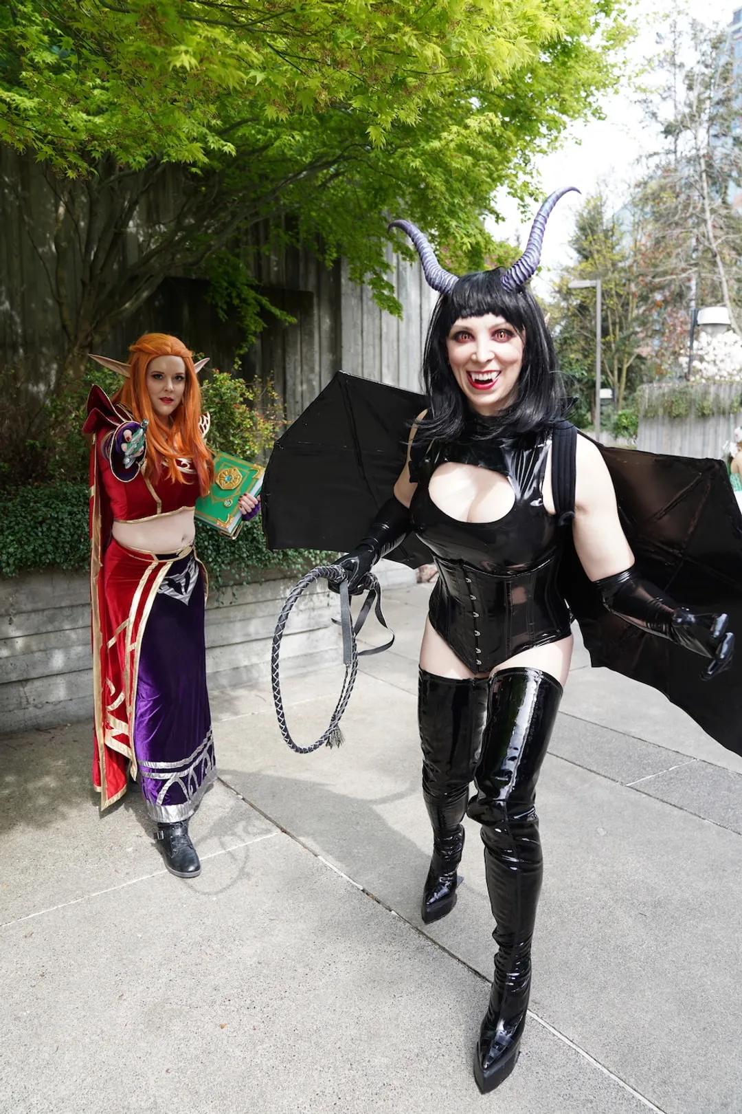 Jerikandra as an original succubus character in black latex with horns and wings, beside another cosplayer outdoors.