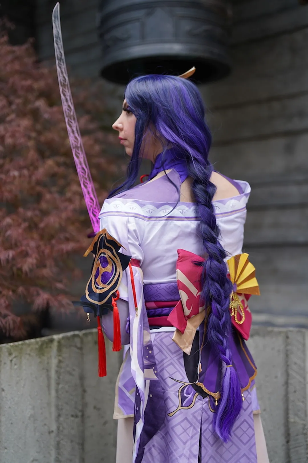 Jerikandra as Raiden Shogun from Genshin Impact, seen from behind with a long purple braid, kimono and drawn sword.