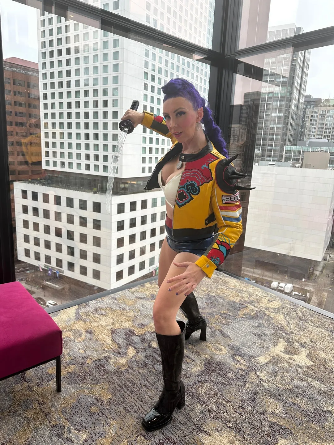 Jerikandra as Rumi from KPop Demon Hunters with a purple braid, yellow and red jacket and black boots, by a high-rise window.